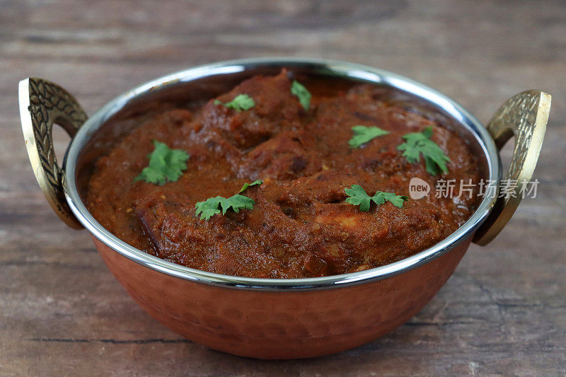 木桌的形象是卡扎伊(kadhai)烹饪锅/盛满自制鸡肉布娜(bhuna)的碗，绿色香菜叶装饰，木纹背景，聚焦前景